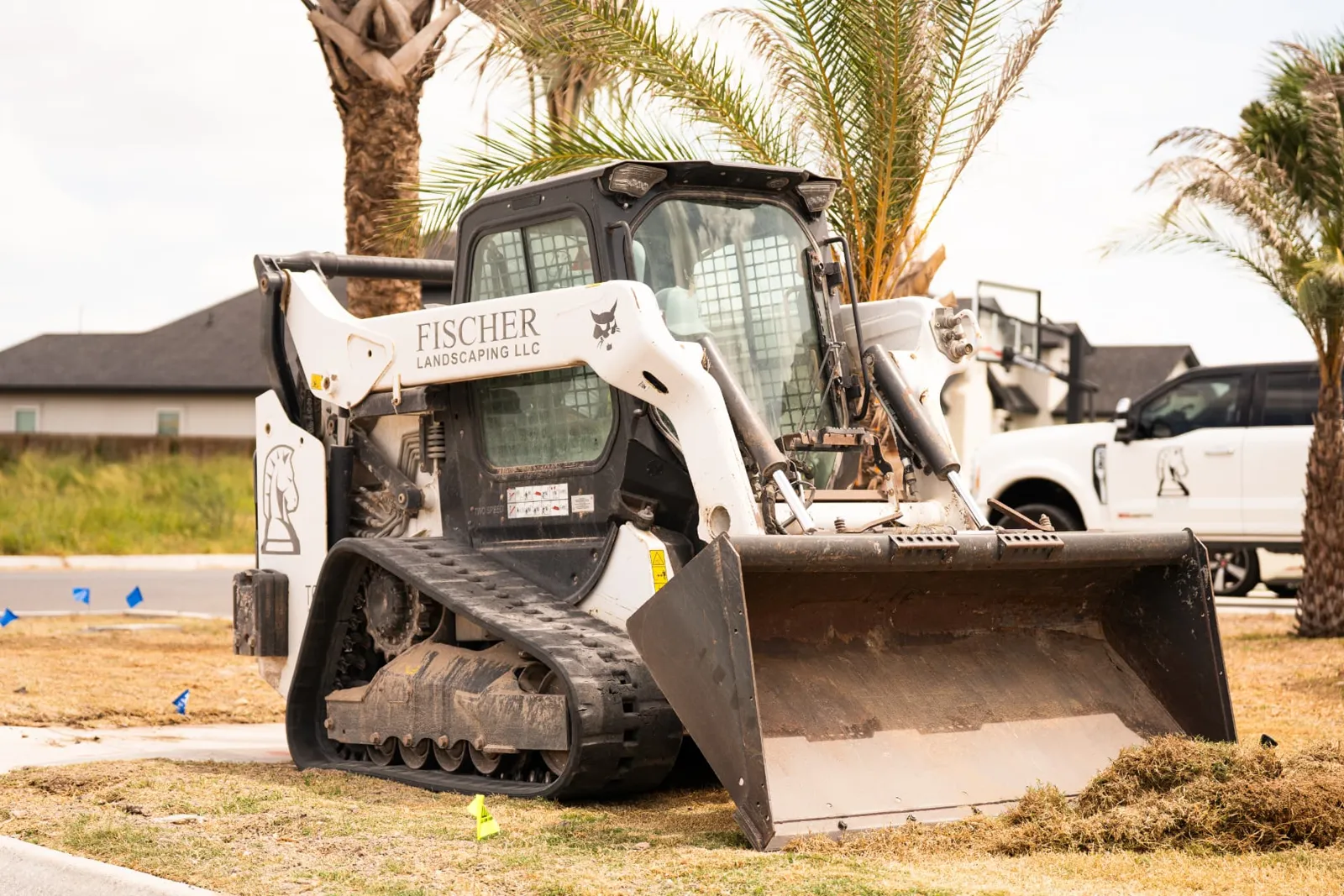 Fischer Landscaping track loader clearing sod beneath palm trees