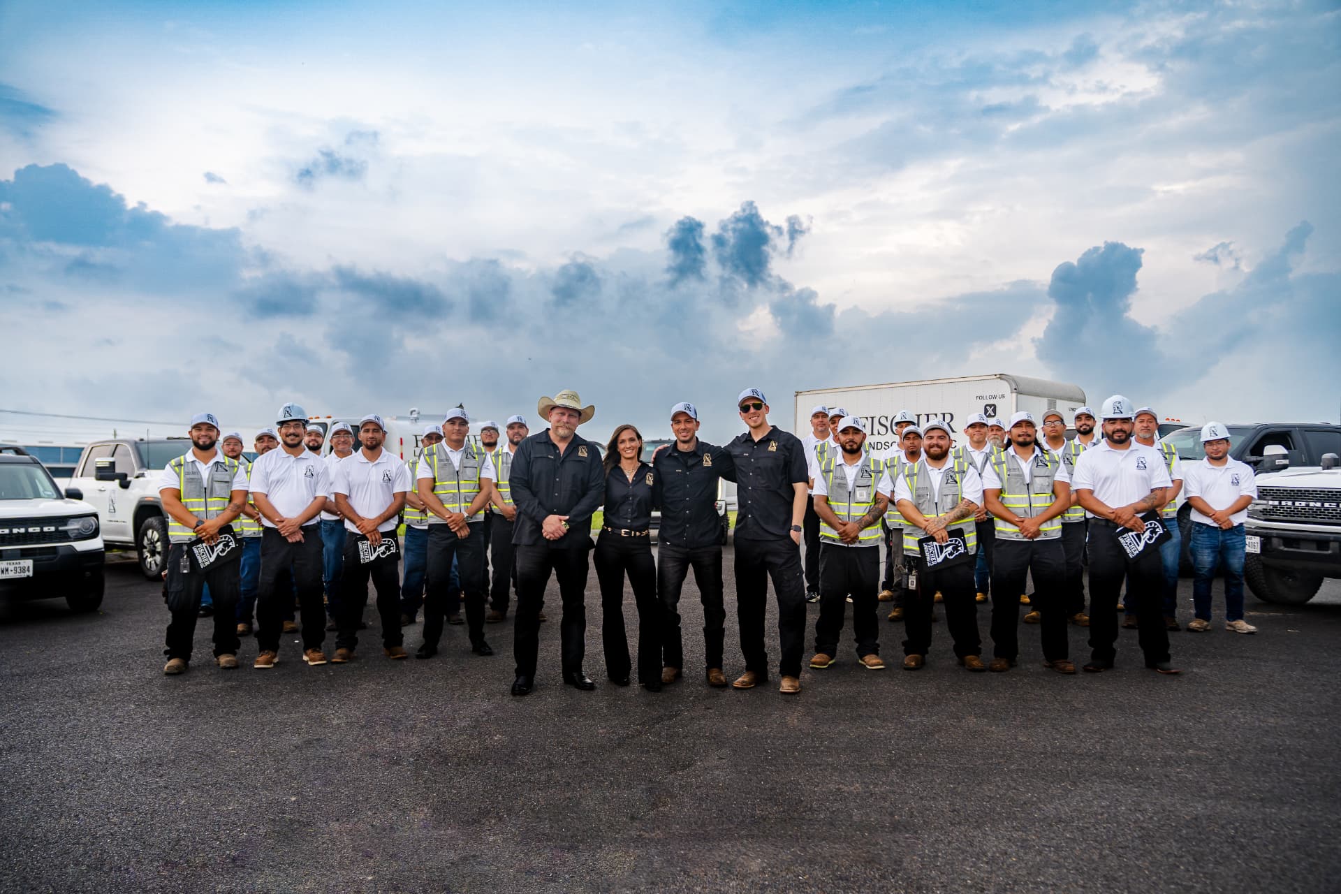 Fischer Landscaping leadership and crew standing together with company trucks under a Texas sky
